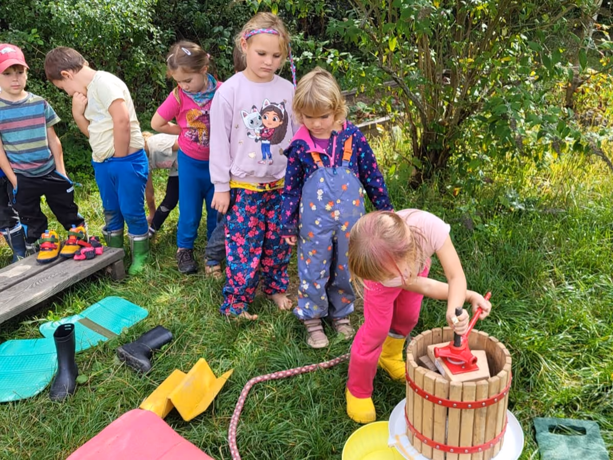 Děti z Devětsilu sledují, jak spolužačka lisuje jablka na ručním lisu