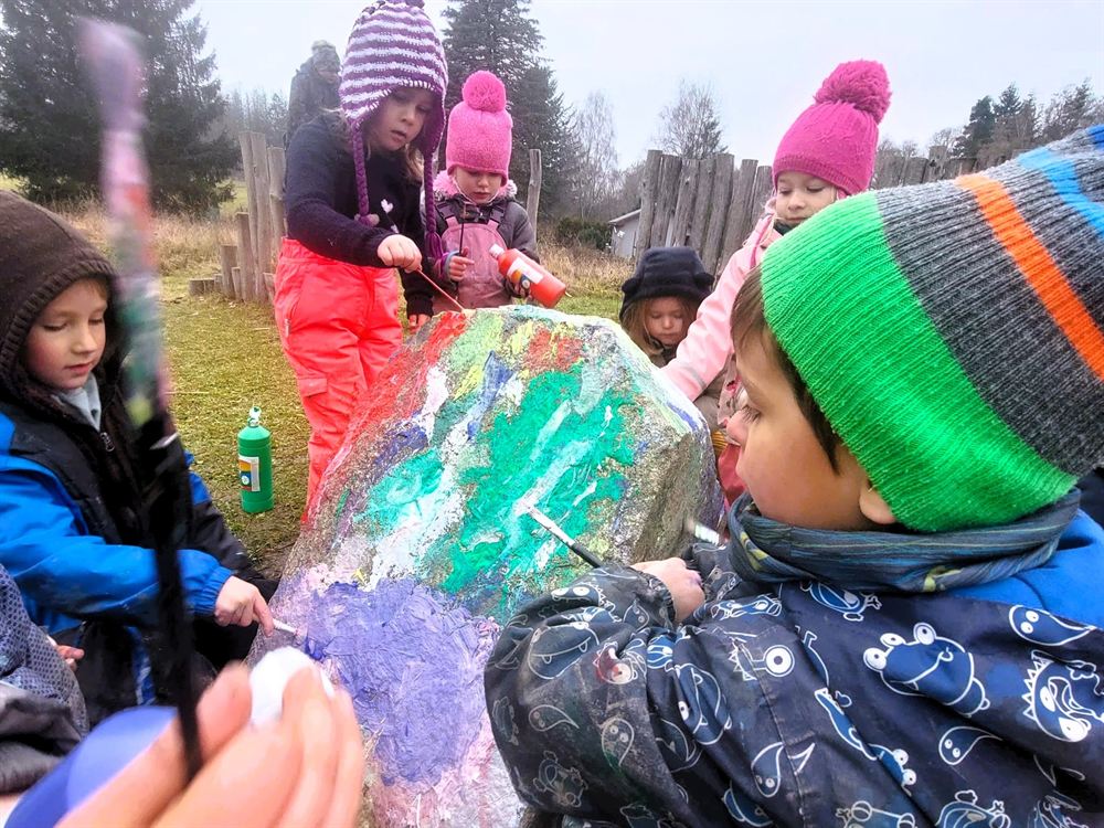 Děti společně barevně malují velký kámen na zahradě