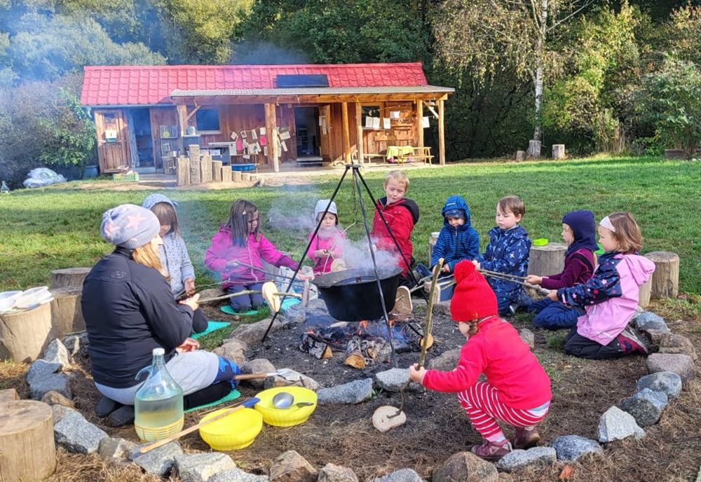 Děti sedí u ohniště a vaří v kotlíku na ohni