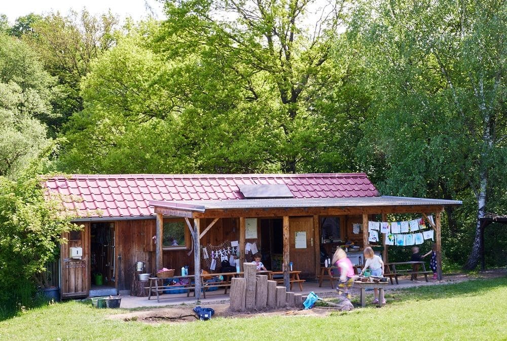 Dřevěný domeček s krytou terasou na louce — zázemí lesní mateřské školy Devětsil
