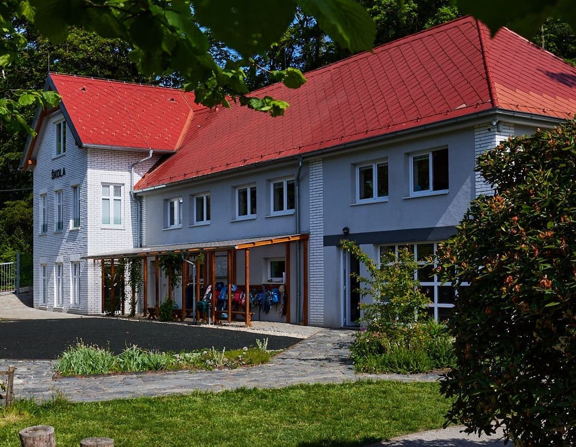 Budova školy Devětsil s červenou střechou v zeleni
